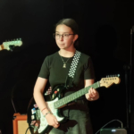 Девочка с гитарой выступает перед зрителями на отчетном концерте.